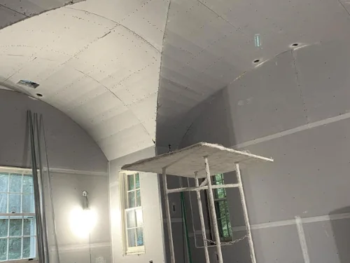 Groin-vaulted ceiling and walls covered in blueboard, with a rolling work platform in the room