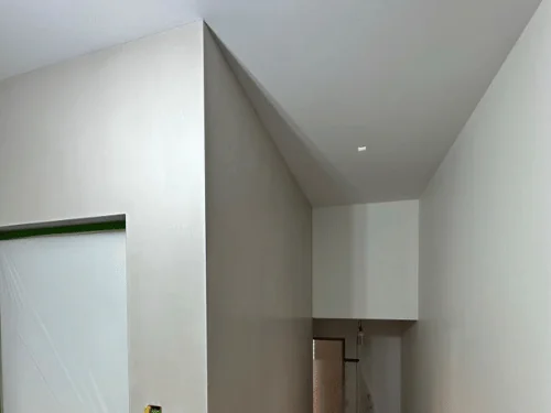 Tall hallway walls and a stepped ceiling in smooth plaster, doorway masked in plastic