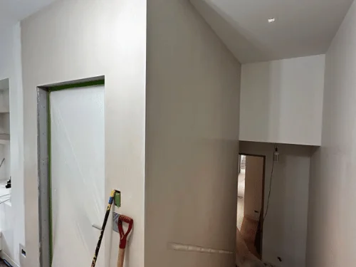 Plastered hallway with a stepped ceiling and a masked doorway, tools resting against the wall
