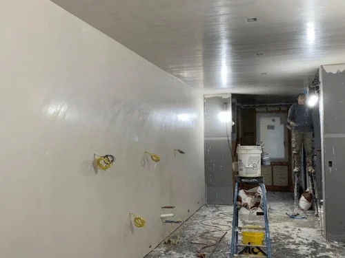 Long hallway with fresh plaster on the walls and ceiling while a plasterer works at the far end
