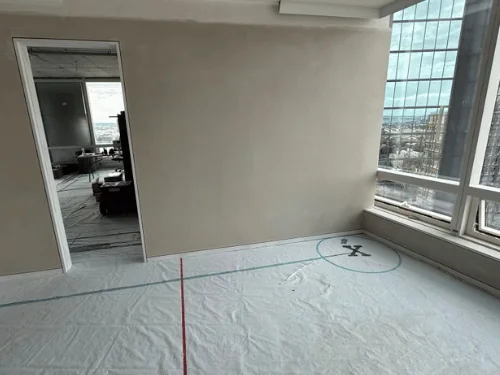 Corner room with plastered walls and floor-to-ceiling windows in a high-rise unit