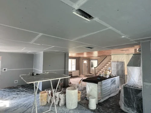 Kitchen and living area with the blueboard ceiling taped, a mixing station set up and cabinets wrapped