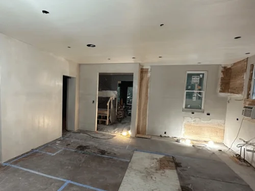 Plastered room opening into the next space, floor protected with taped boards