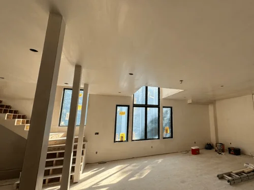 Sunlit open room with plastered walls and ceiling, boxed columns and stairs still in rough framing