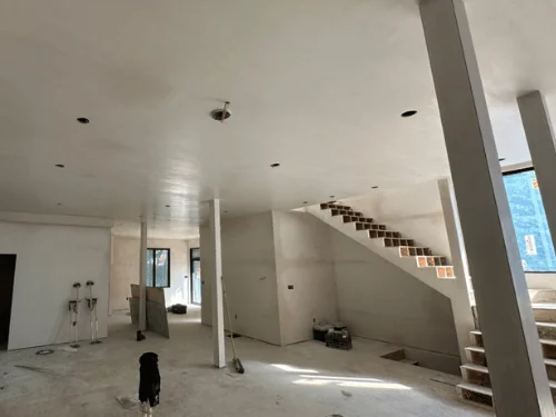 Long open floor with a plastered ceiling, a boxed column and an unfinished staircase