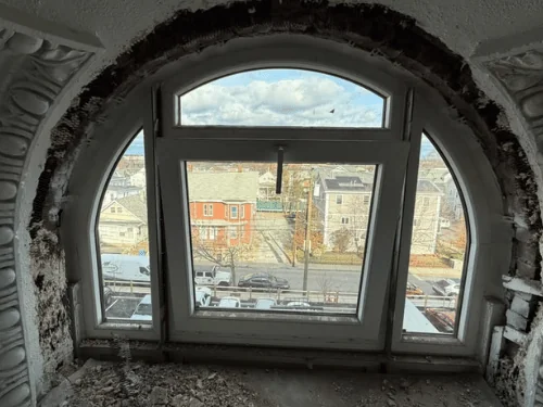Arched window in an old house with damaged ornamental plaster around it, debris on the floor before restoration