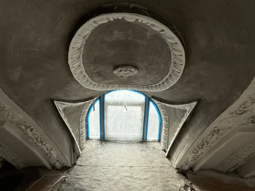 Ornamental plaster medallion and carved brackets around an arched window, walls in gray base coat