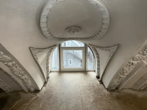Restored ornamental plaster medallion and brackets framing an arched window, finished in white