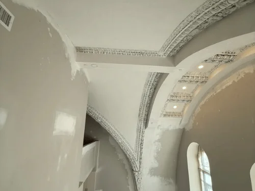 Ornamental plaster ribs and cornice above walls spotted with fresh compound around an arched window