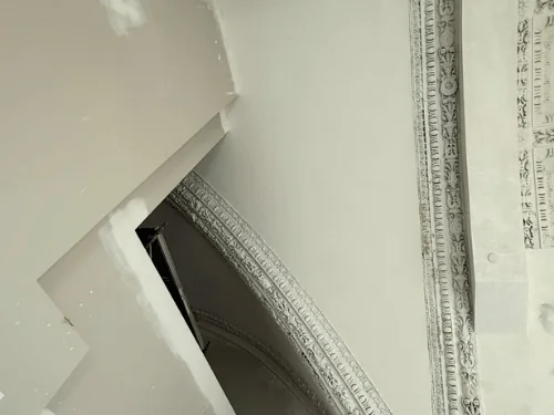 Close view of ornate plaster ribs and cornice beside new board with compound patches
