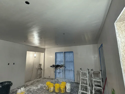 Plastered room with mixing buckets, stepladders and a trash barrel on a covered floor