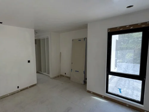 White plaster room with a black-framed window and closet openings, doors waiting to be hung