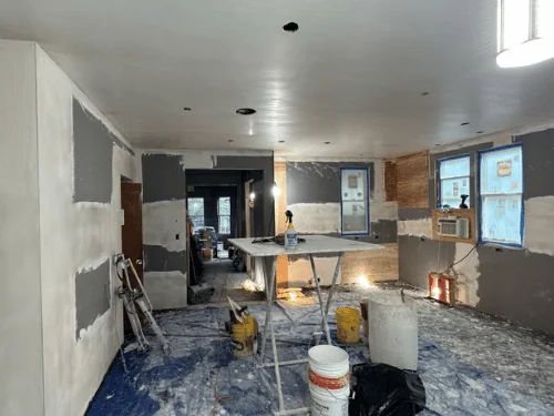 Room mid-coat, fresh plaster going on over blueboard, with mixing buckets and a work table