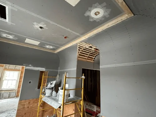 Room in blueboard with taped joints and patched light openings, an arched doorway framed and a scaffold set up