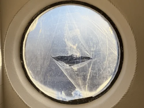 Repaired plaster around a round window with a rope-pattern edge, glass still covered in plastic