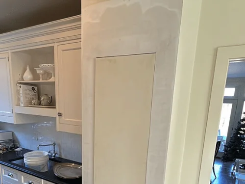 Kitchen wall getting a skim coat, fresh plaster patches over the old surface beside white cabinets