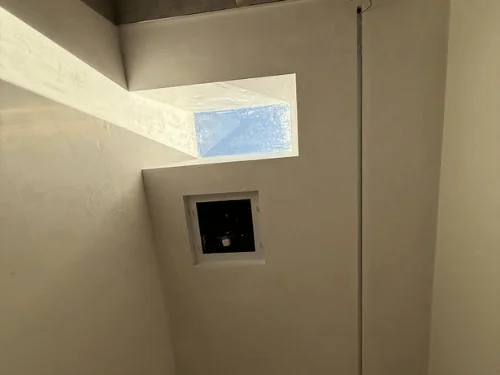 Plastered skylight well cutting through a sloped ceiling above an exhaust fan opening