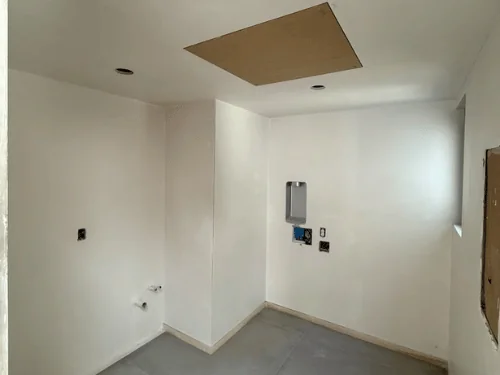Small room with smooth white plaster walls and a ceiling access panel waiting for its cover