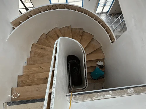 Spiral staircase seen from above, its curved walls finished in plaster around oak treads