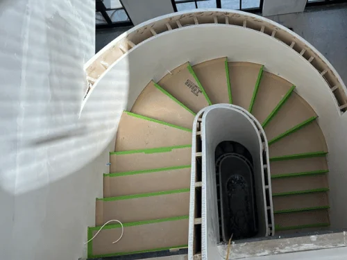 Oval spiral staircase seen from above, curved plaster walls around treads still covered for protection