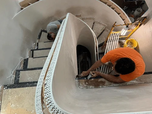 Plasterers working on a curved stair wall seen from above, flexible corner bead set along the edge