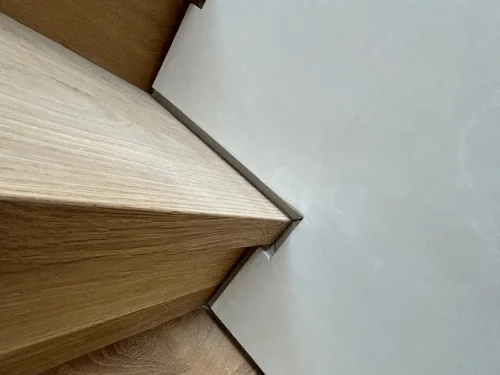 Oak stair treads meeting a smooth plaster wall with a tight, clean edge