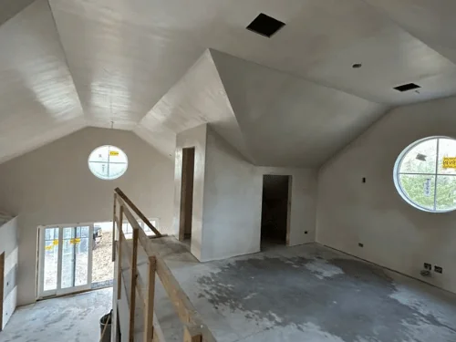 Open upstairs room with angled ceilings and two round windows, walls and ceilings in fresh plaster