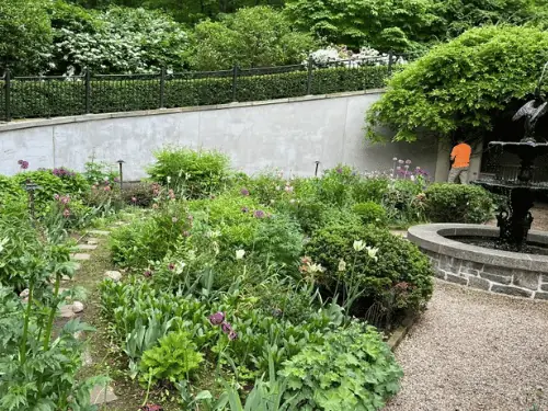 Garden retaining wall finished in smooth gray stucco beneath an iron fence, a fountain in front