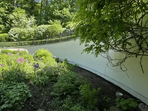 Curved garden retaining wall finished in smooth cream stucco below an iron fence