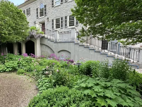 Stone house above a garden, its exterior stair walls and lower arches finished in smooth stucco